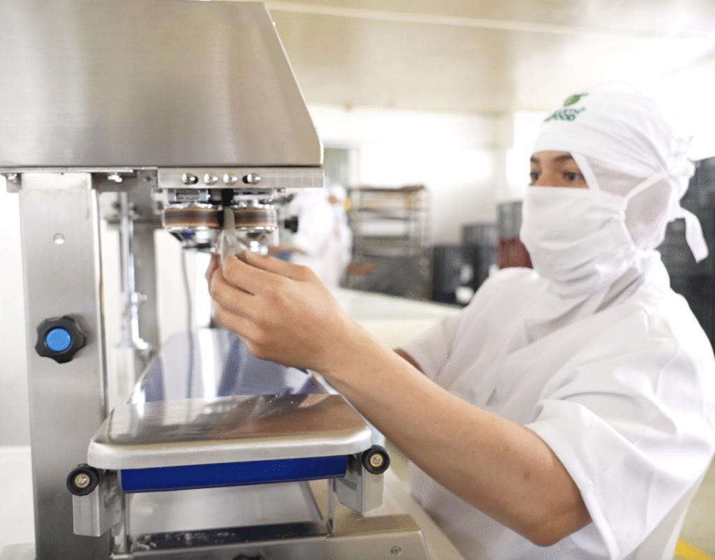 La Huerta de Oriente employee operating a vertical industrial sealing machine, handling packaged products in a food processing facility